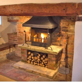 A re-modelled fireplace with raised hearth on brick plinths including log store. Thermovent high performance wood burning open fire with stel canopy,