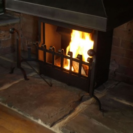 Close up of Anniversary edition dog irons and fire grate with hand forged swan neck ball top dog irons with horse shoe feet.