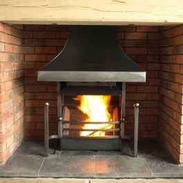 High polish steel canopy Thermovent convecting open fire with tall slender dog irons featuring ball tops. Square bar bow front grate.