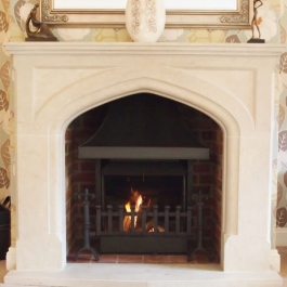 Stone fire surround open fireplace with Thermvoent convection fire featuring steel canopy with cast Fleur des Lis dog irons and scroll top grate front.